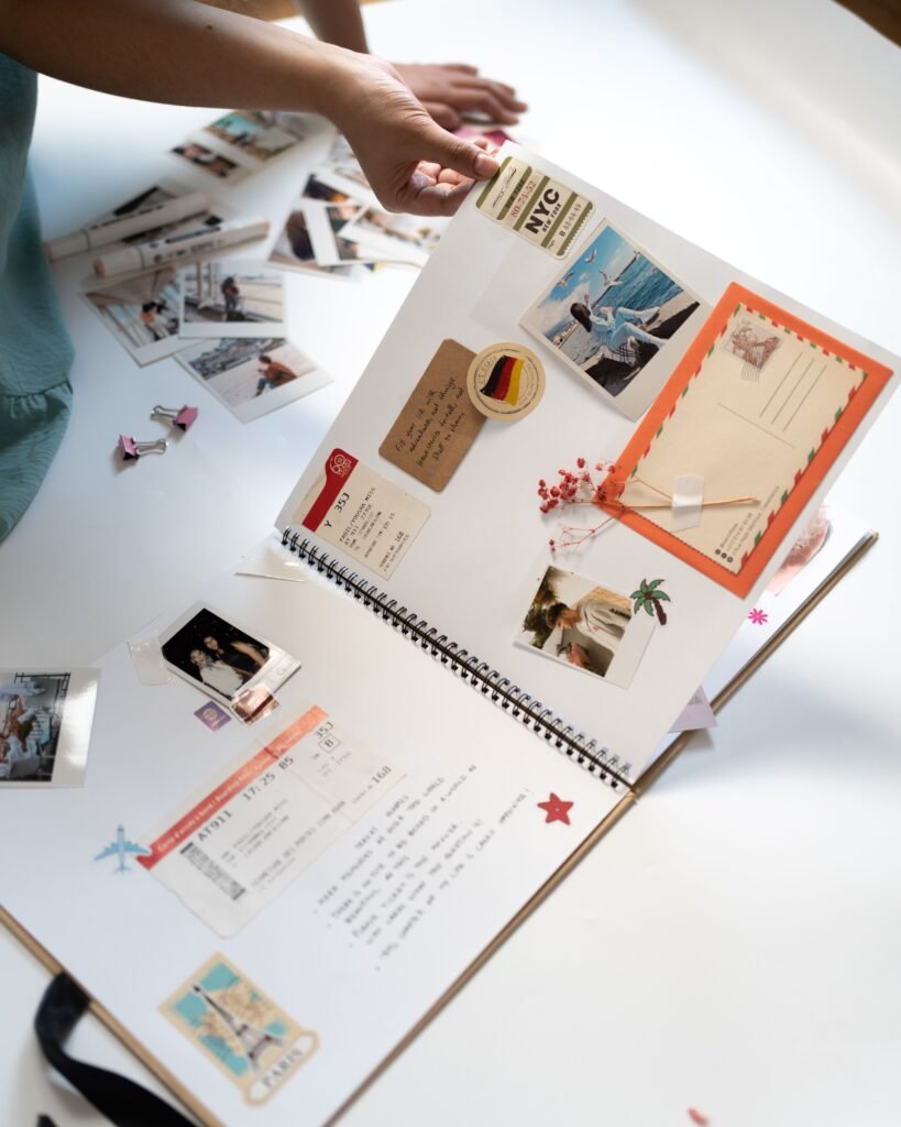 A person crafting a scrapbook with personal photos, postcards, and mementos on a white background.